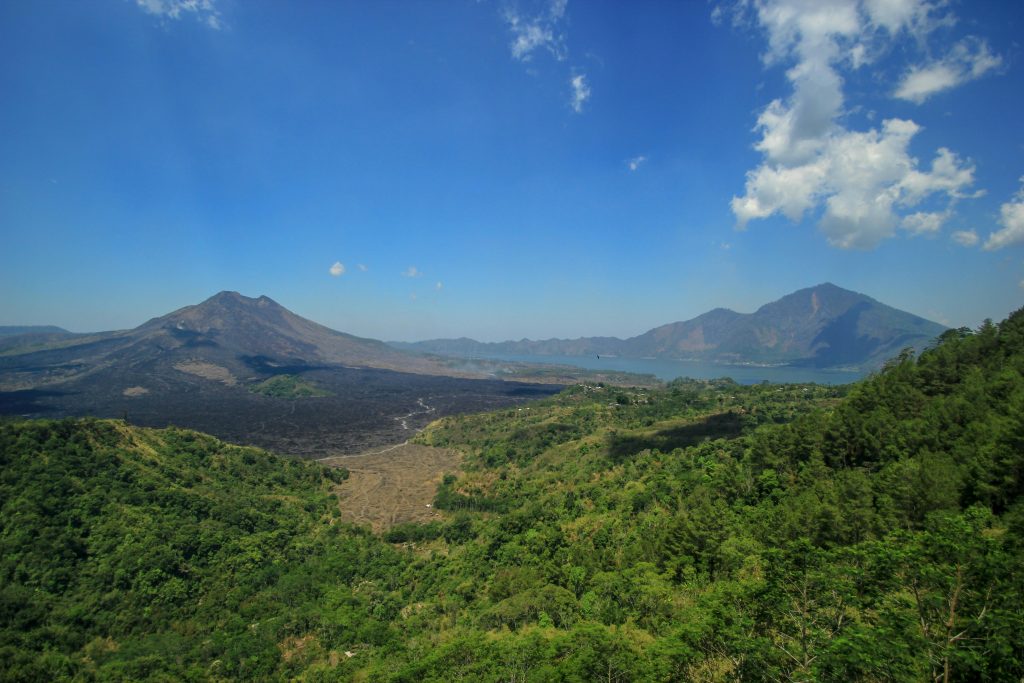 Breathtaking aerial view of Mount Batur and lush valley in Bali with clear blue skies.